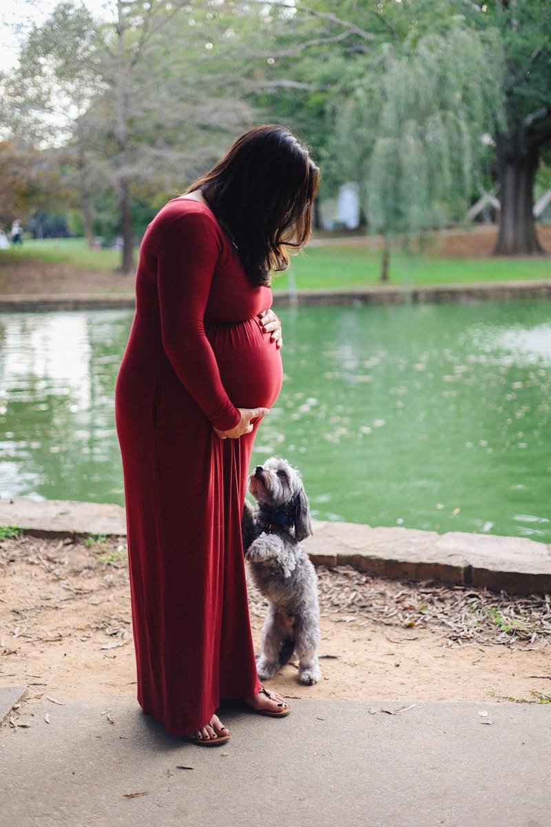 Une femme enceinte et son chien posent au bord d'un lac.
